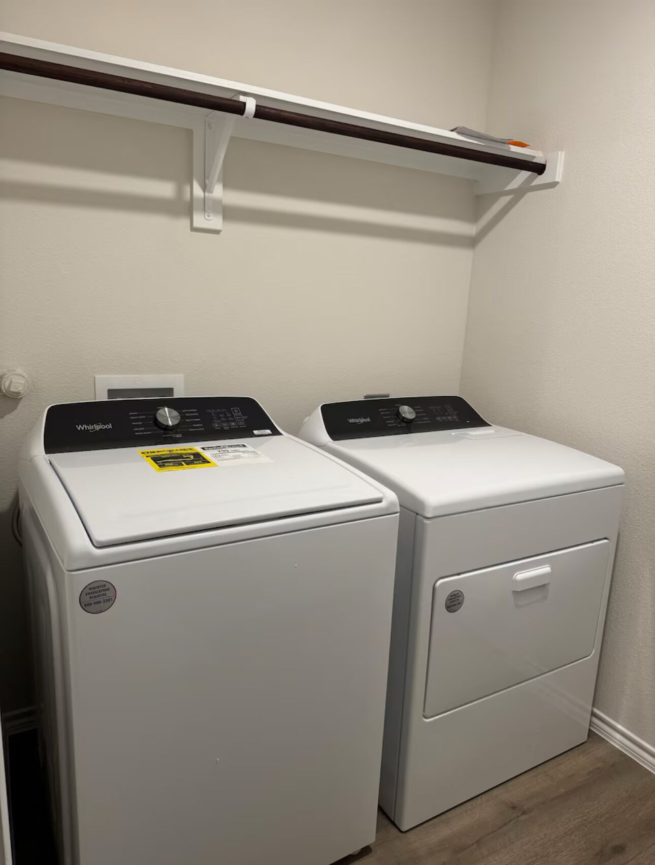 Un lavadero con dos lavadoras Whirlpool de carga frontal y un estante blanco encima.