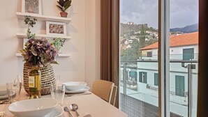 A dining area with a table set for two, a vase of flowers, and a view of a cityscape through large windows. - Acanto Loft by Atlantic Holiday (Funchal)