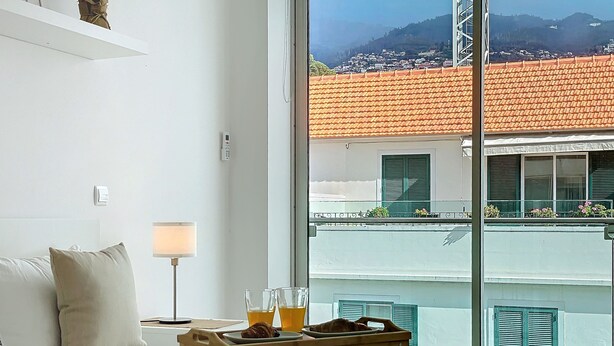 A bedroom with a bed, bedside lamp, and a breakfast tray with croissants and orange juice. - Acanto Loft by Atlantic Holiday (Funchal)