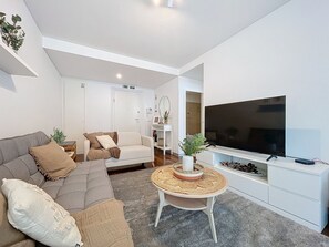 A modern living room with a grey sofa, a white armchair, a round coffee table, and a large flat-screen TV. - Acanto Loft by Atlantic Holiday (Funchal)