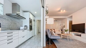 A modern kitchen with white cabinets and a marble countertop, a living area with a sofa and a TV, and a hallway connecting the two spaces. - Acanto Loft by Atlantic Holiday (Funchal)