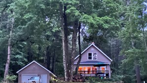 A cabin with a garage and a covered porch, surrounded by dense forest.