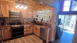 A rustic kitchen with wooden cabinets, a stainless steel stove, and a large window. - Cabin in the TreeTops! 4 Level a-frame cabin, with 5 levels of decks (Lancaster)