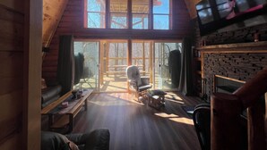 A cozy cabin interior with a wooden ceiling, a fireplace, a television, and a large window overlooking a deck. - Cabin in the TreeTops! 4 Level a-frame cabin, with 5 levels of decks (Lancaster)