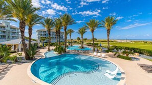 A swimming pool with palm trees, lounge chairs, and a view of the ocean. - Bayfront 4BR Retreat in Pointe West with Hot Tub Sleeps 12 (Galveston)