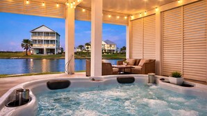 A hot tub area with a view of a lake and a building in the background. - Bayfront 4BR Retreat in Pointe West with Hot Tub Sleeps 12 (Galveston)