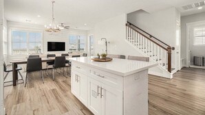 A spacious kitchen with a central island, a dining area with chairs, a large window, and a staircase. - Bayfront 4BR Retreat in Pointe West with Hot Tub Sleeps 12 (Galveston)
