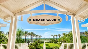 A beach club sign with palm trees and a clear sky in the background. - Bayfront 4BR Retreat in Pointe West with Hot Tub Sleeps 12 (Galveston)