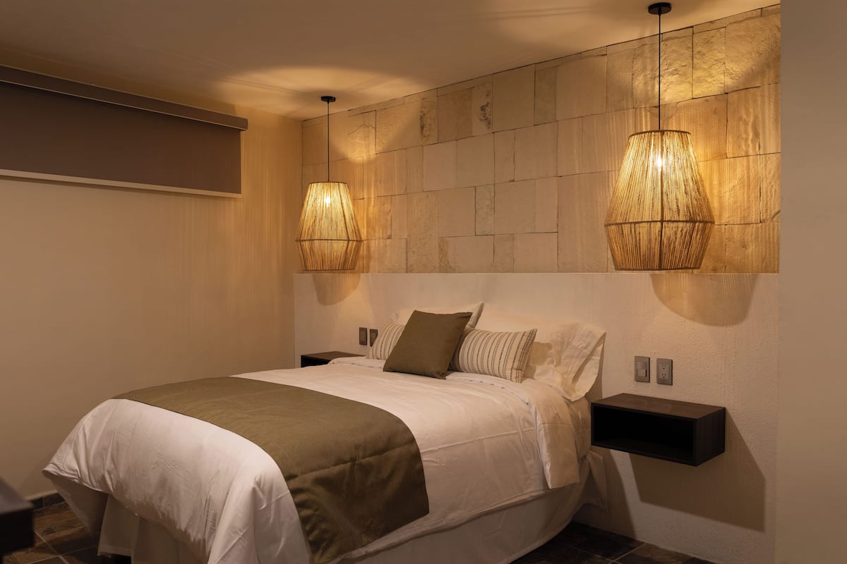 Une chambre à coucher moderne avec un grand lit, deux tables de chevet et un luminaire fixé au mur.