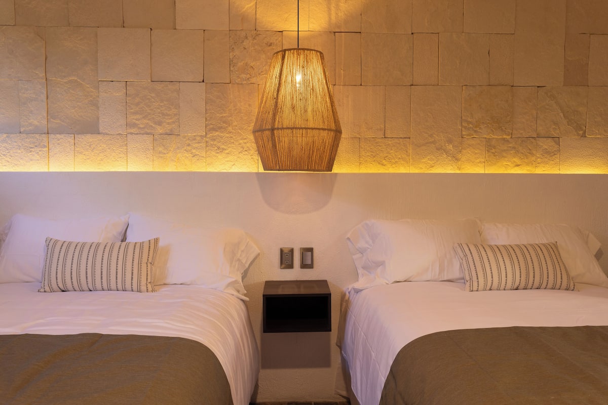 Une chambre d’hôtel avec deux lits, une lampe fixée au mur et une petite table de chevet placée entre les deux.