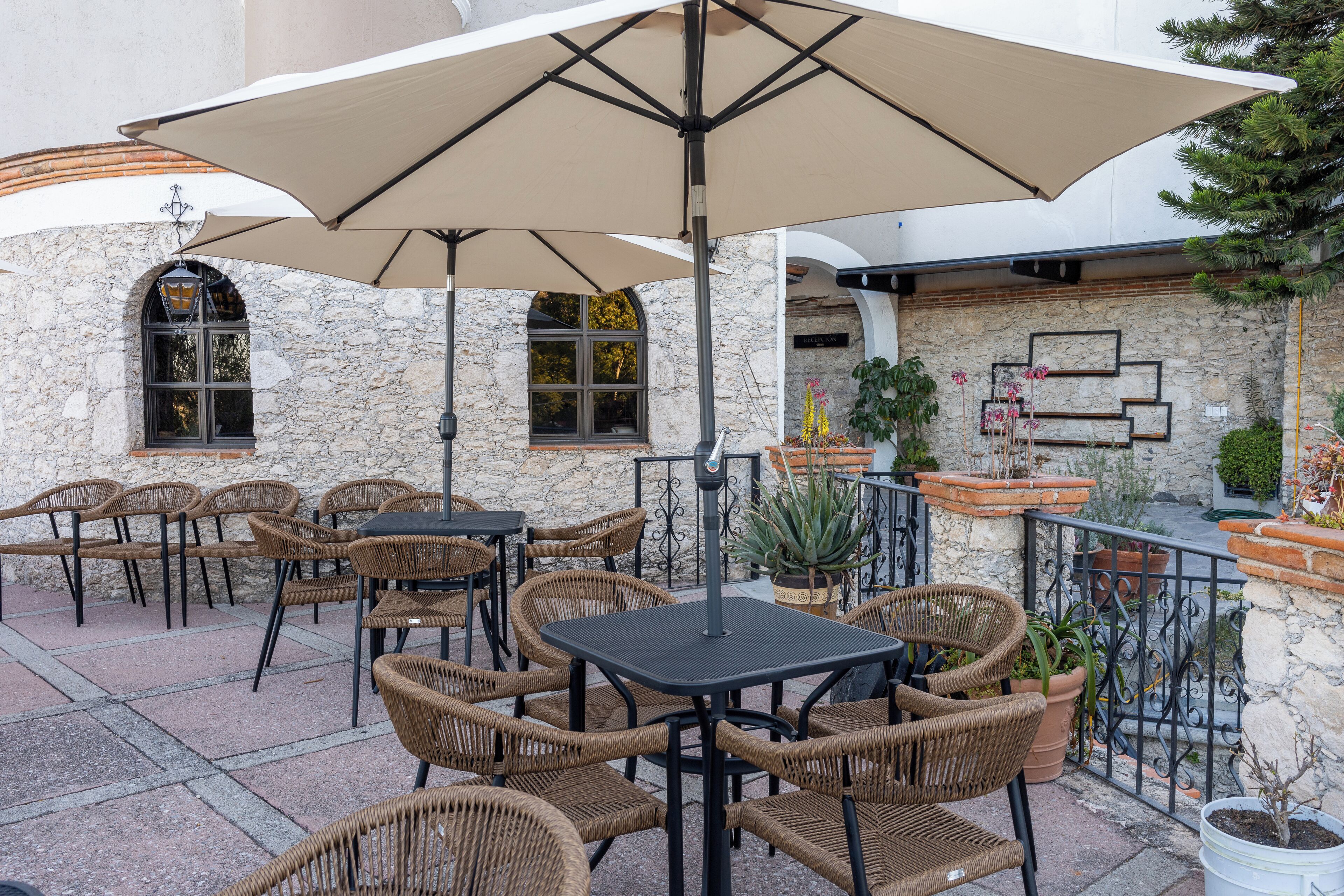 An outdoor patio with wicker chairs and tables, stone walls, and potted plants.