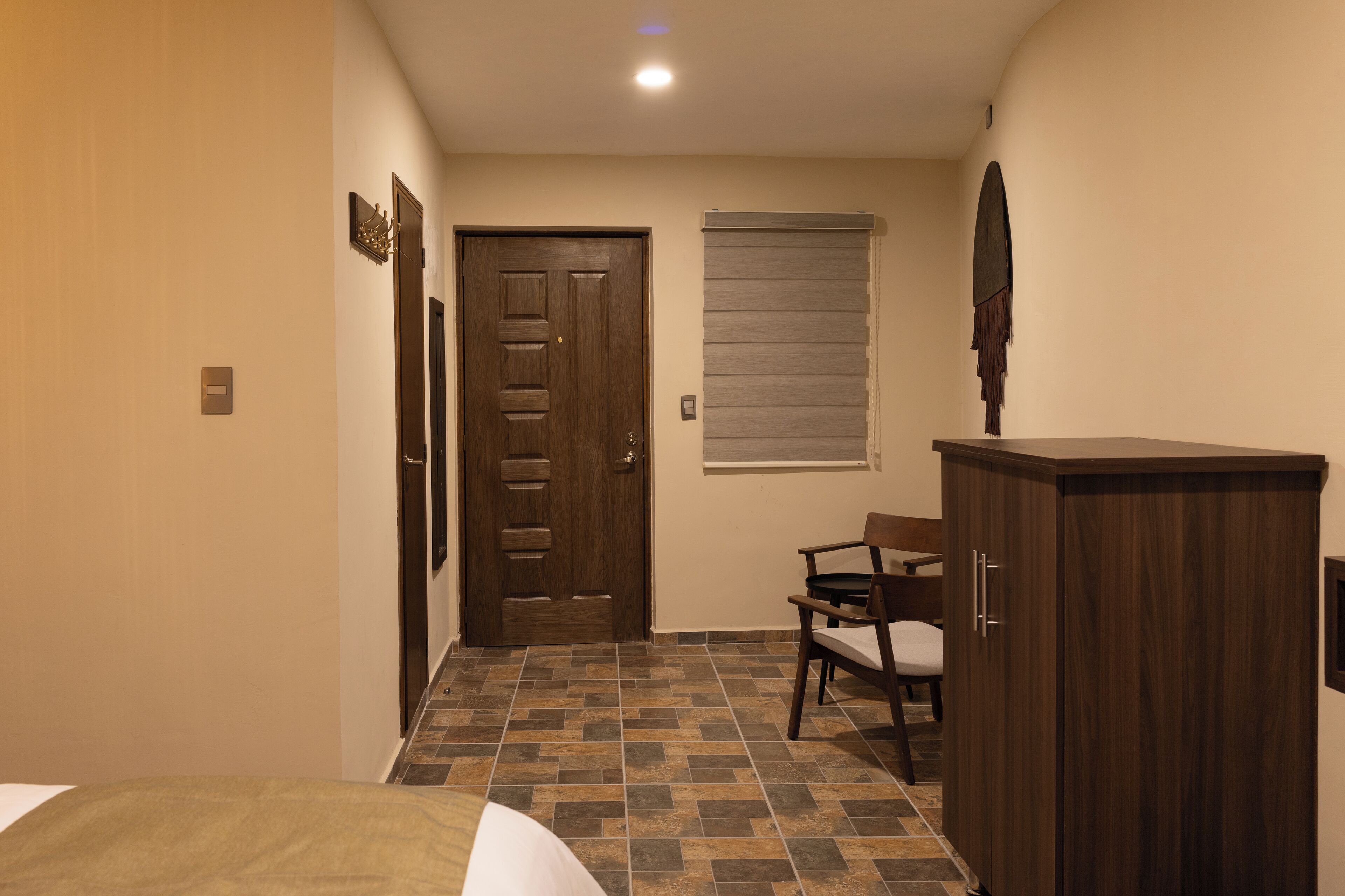 Une chambre d’hôtel avec un lit, une armoire en bois, une chaise et une porte avec une fenêtre.