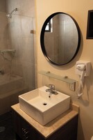 Un baño con cabina de ducha de vidrio, un lavamanos blanco con espejo y un secador de pelo en la pared.