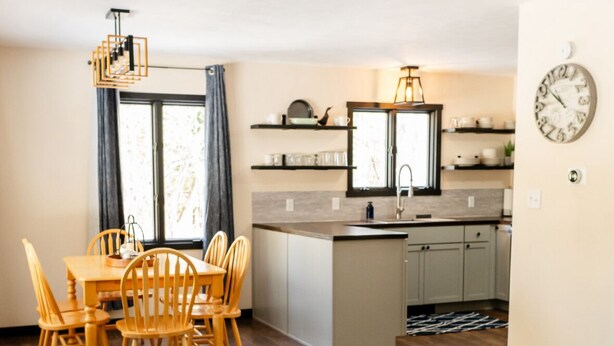 Una sala de estar moderna con un sillón gris, una mesa de centro redonda de madera, y un comedor con sillas y una mesa de madera.
