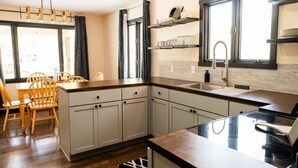 Una cocina moderna con armarios blancos, una mesa de comedor de madera y un ventanal grande.