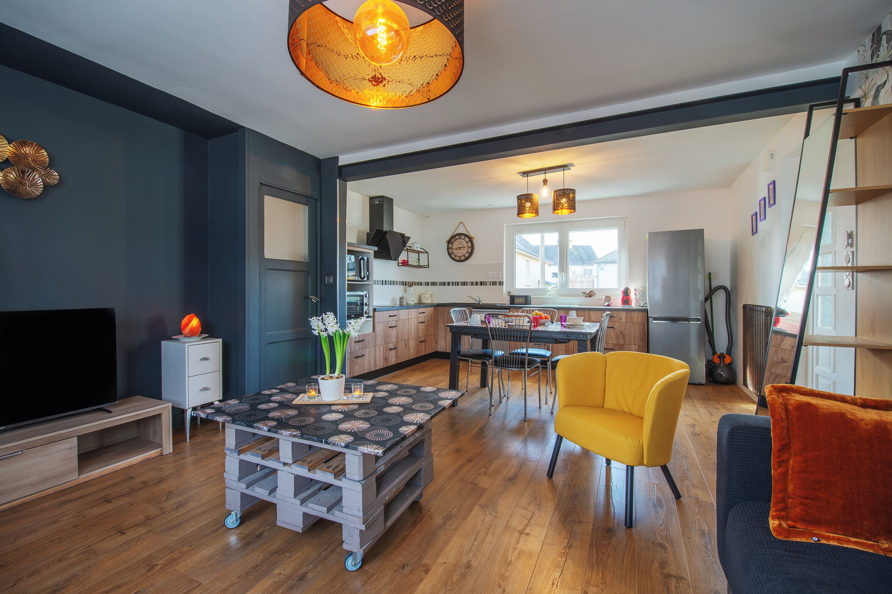 Un salon moderne avec un téléviseur, une table basse, un fauteuil jaune et un canapé.