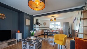 A modern living room with a TV, a coffee table, a yellow armchair, and a sofa. - Le Jovia - Cour extérieure - Wifi (Laval)