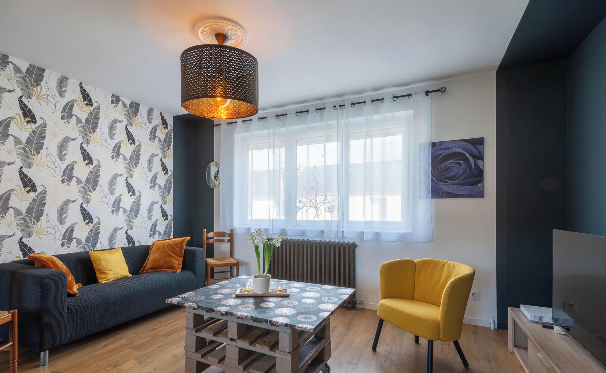 Un salon avec un canapé, un fauteuil jaune et une table recouverte d’une nappe à motifs.