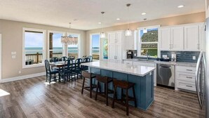 A spacious kitchen with a large island, white cabinets, and a view of the ocean through large windows. - Beachfront | Hot Tub | Putt Putt | Fire Pit (Gilchrist)