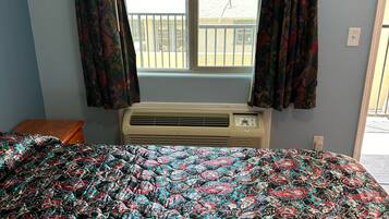 Una habitación con una cama cubierta por una colcha estampada, una ventana con cortinas y un equipo de aire acondicionado.
