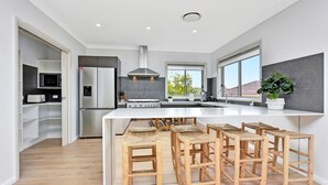 A modern kitchen with a central island, built-in appliances, and a large window. - Finns at Caves Beach Resort (Caves Beach)