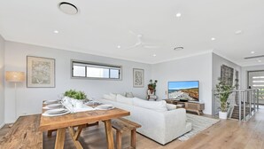 A spacious living area with a dining table set for six, a white sofa, and a television. - Finns at Caves Beach Resort (Caves Beach)
