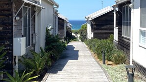 A pathway leading to beachside cabins with a view of the ocean. - Finns at Caves Beach Resort (Caves Beach)