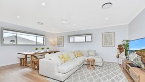 A modern living space with a sectional sofa, dining table, and a flat-screen TV. - Finns at Caves Beach Resort (Caves Beach)