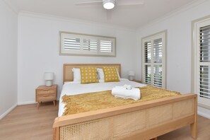Een slaapkamer met een houten bed, witte beddengoed, een nachtkastje met een lamp en een raam met zonwering.