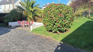 A paved patio with outdoor seating, a well-maintained hedge, and a palm tree. - new house, beach at 5 minutes, 3 bedrooms, large garden, terrace, bike provided. (Pont-Croix)