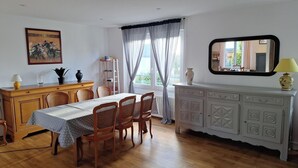 A dining area with a wooden table and chairs, a white cabinet with decorative patterns, a mirror, and a painting on the wall. - new house, beach at 5 minutes, 3 bedrooms, large garden, terrace, bike provided. (Pont-Croix)