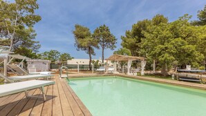 A pool area with wooden deck, lounge chairs, and a gazebo.