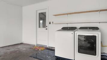 A laundry room with two washing machines, a door, and a wooden shelf above the machines.