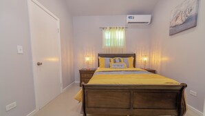 A bedroom with a wooden bed, two bedside tables with lamps, a window with sheer curtains, and an air conditioning unit on the wall. - Beautiful 1-bedroom apartment in amazing Buckleys with AC, WiFi (Buckleys)