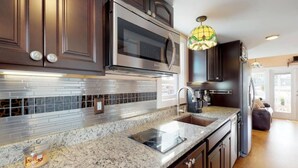 A modern kitchen with dark wood cabinets, stainless steel appliances, a granite countertop, and a decorative hanging light fixture.