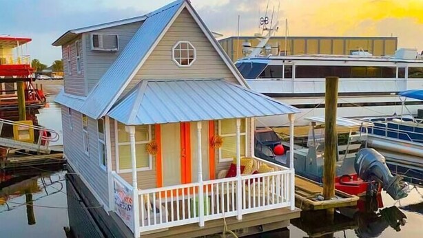 A houseboat with a balcony, docked at a marina with other boats.
