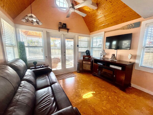 A living room with a leather sofa, a ceiling fan, a TV, and a kitchen area with a sign reading "Dine & Relax". - Famous Houseboat (Sanford)