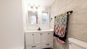 A bathroom with a white vanity, a bathtub, and a toilet. - Fully remodeled cozy mobile home in charming Zephyrhills with AC, WiFi (Zephyrhills)