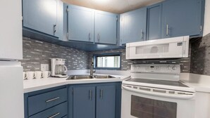 A compact kitchen with blue cabinets, a white microwave, and a stove. - Fully remodeled cozy mobile home in charming Zephyrhills with AC, WiFi (Zephyrhills)