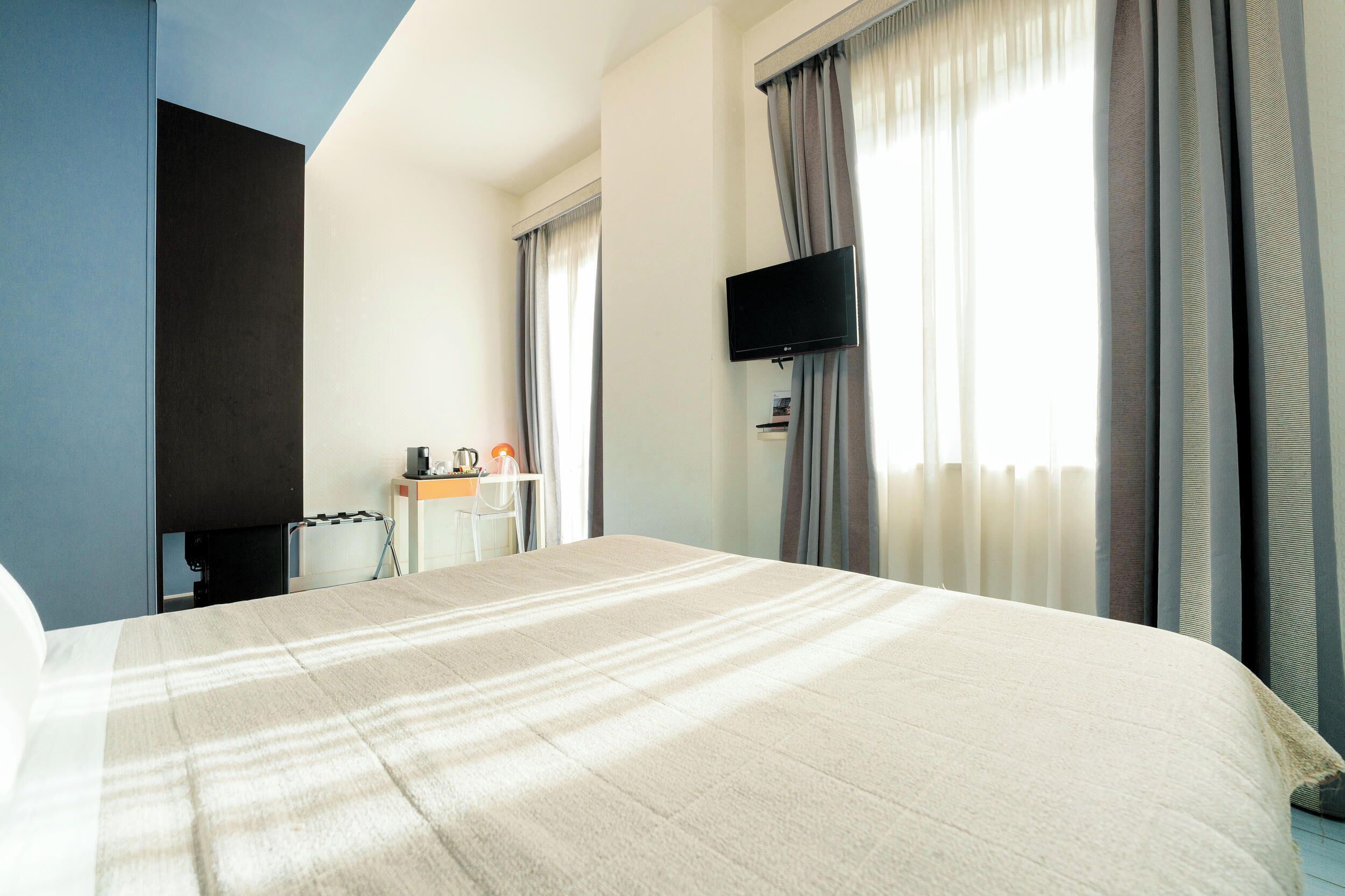 Une chambre d’hôtel dotée d’un grand lit, d’un téléviseur à écran plat fixé au mur, d’un bureau avec une chaise et d’une fenêtre avec des rideaux.