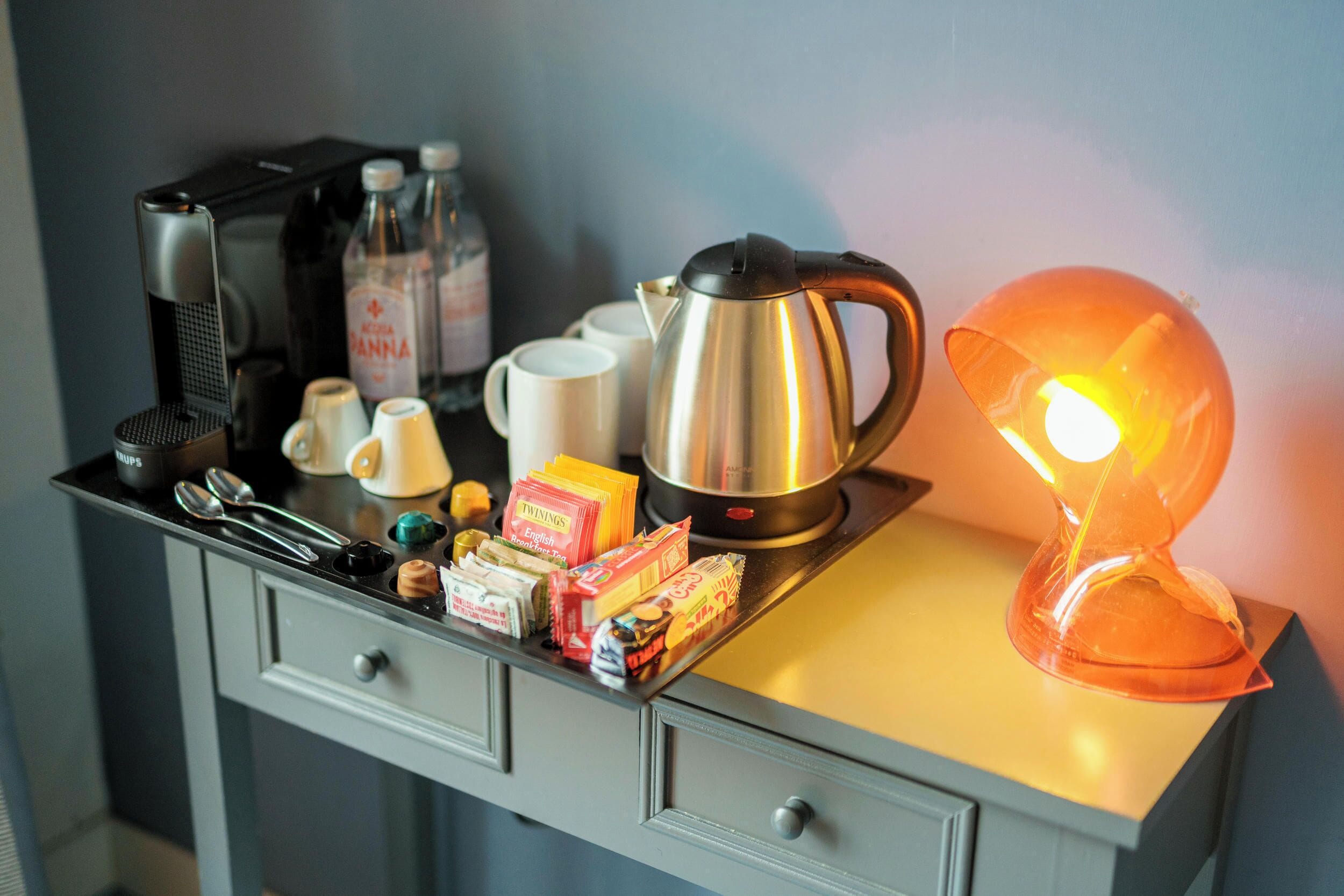 A kitchenette with a coffee maker, kettle, and a lit orange lamp.