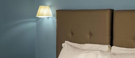 A neatly made bed with white linens in a room with blue walls and a wall-mounted lamp.