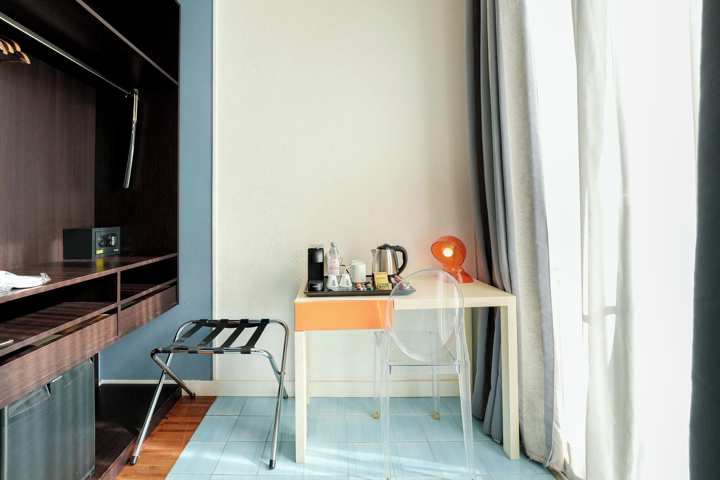 A compact hotel room with a desk, chair, and a small kitchenette area.