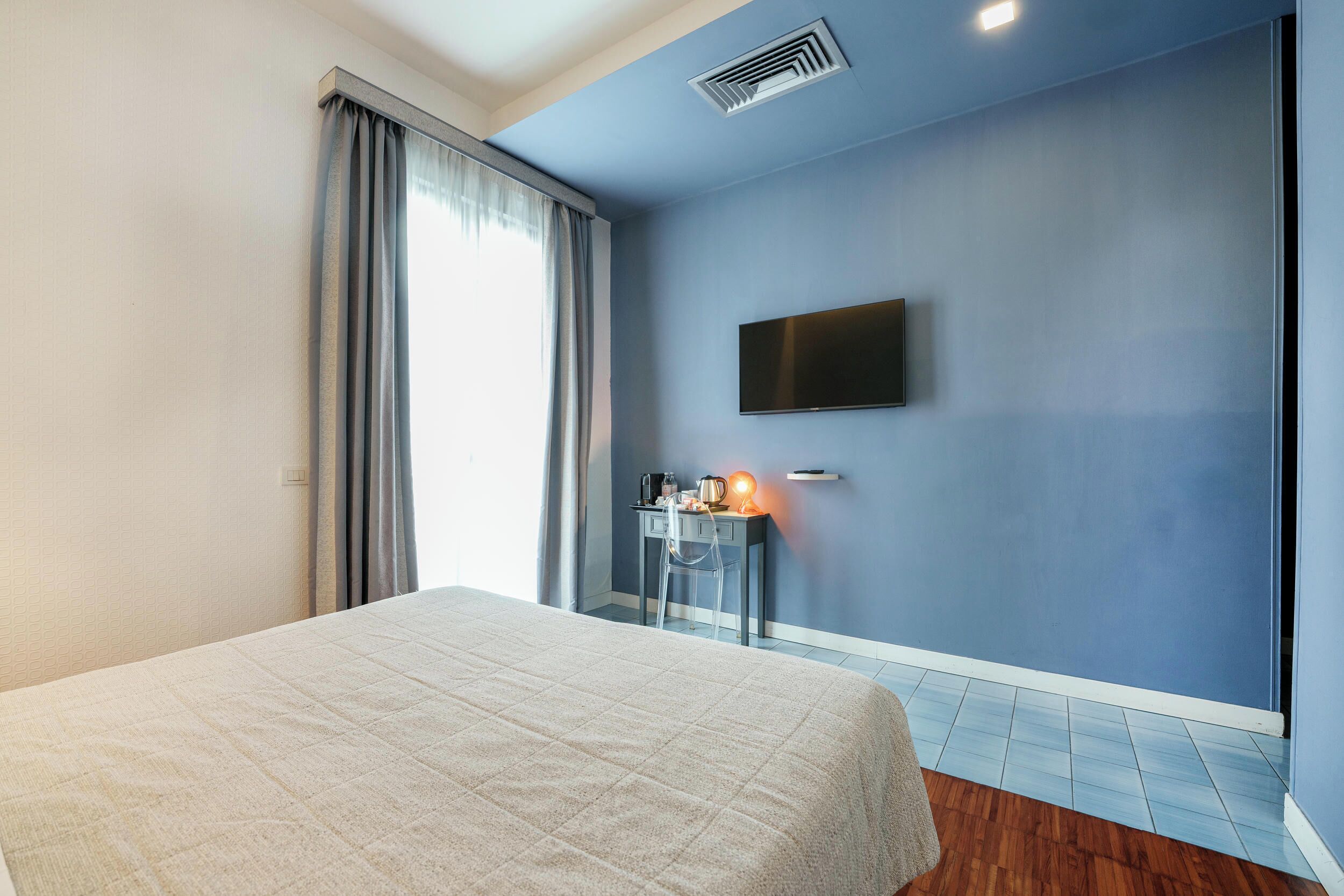 Hotelkamer met een bed, bureau met lamp, flatscreen-tv en raam met gordijnen.