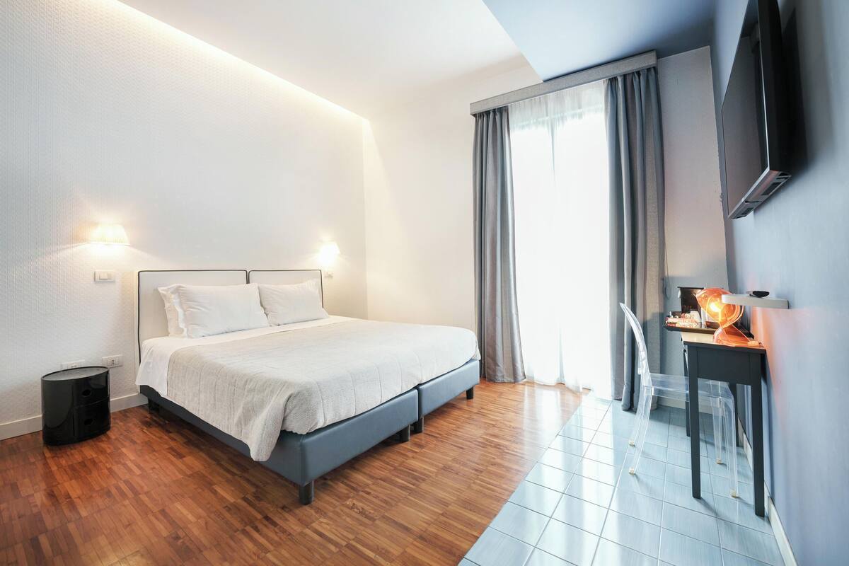 A modern bedroom with a bed, bedside tables, a desk, and a TV.