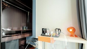 Une chambre d’hôtel compacte comprenant un coin cuisine, un petit réfrigérateur, un four à micro-ondes, une machine à café et un bureau avec une chaise.