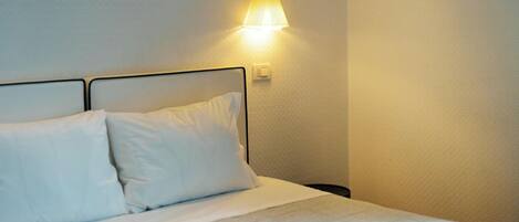 A neatly made bed with white linens and pillows, a wall-mounted lamp, and a textured wall.
