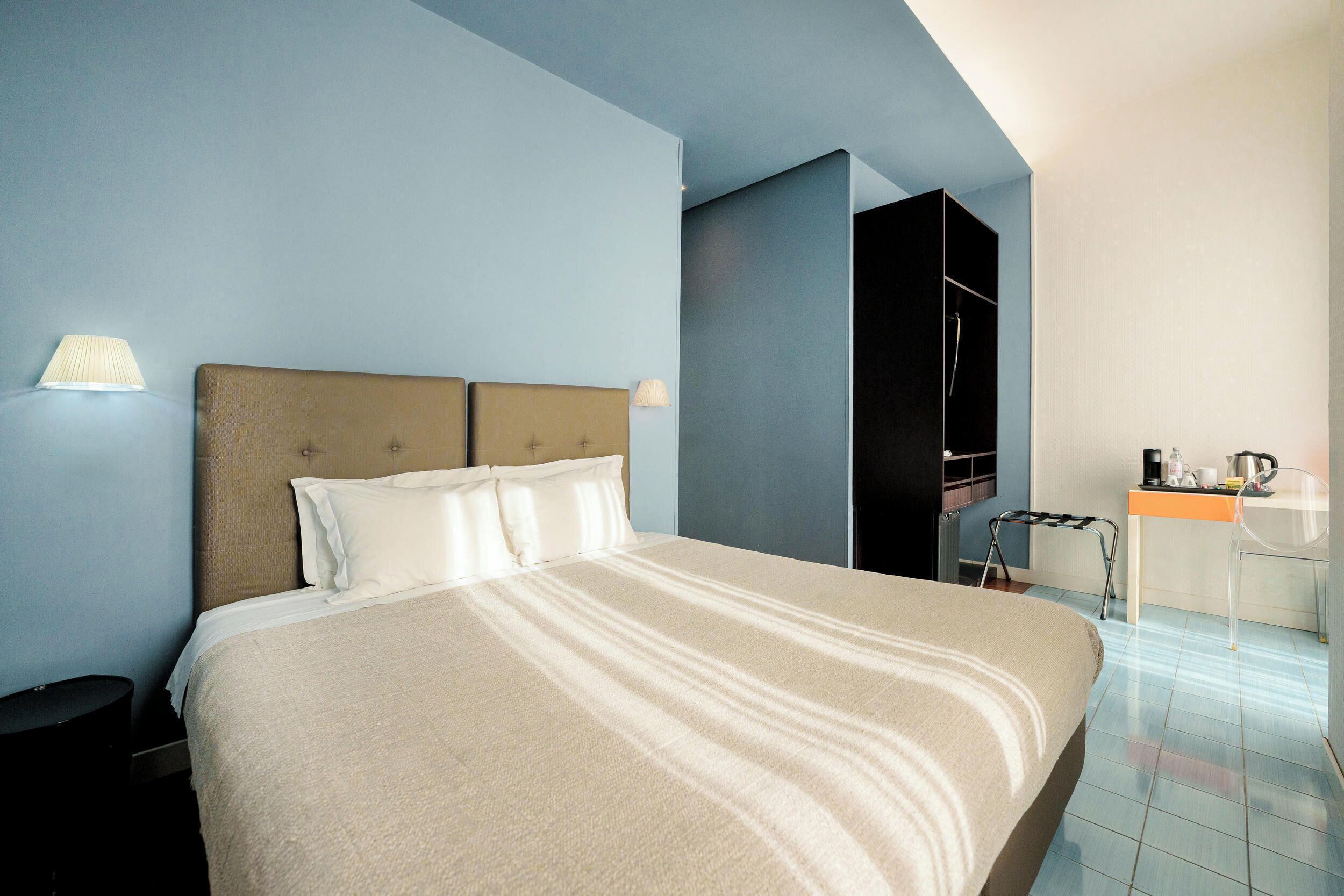 A hotel room with a large bed, a desk with a chair, and a wardrobe.