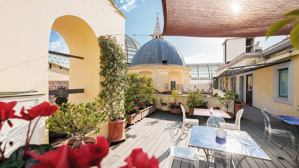 Une terrasse sur le toit, avec une table et des chaises, des plantes en pot et une structure en forme de dôme en arrière-plan.
