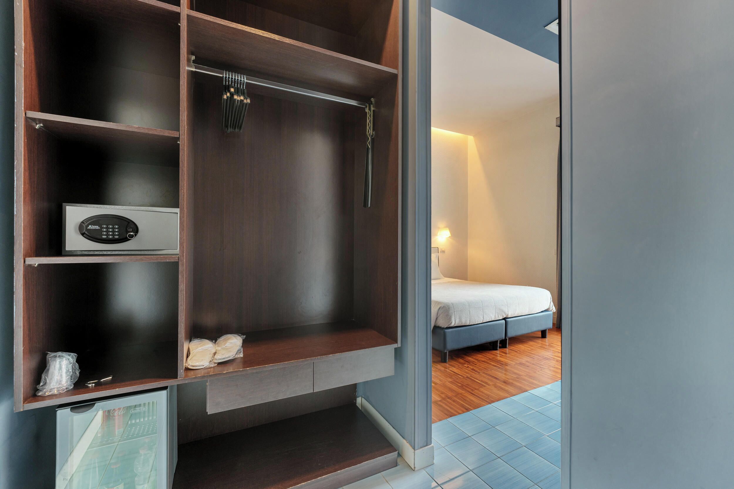 Ein modernes Hotelzimmer mit eingebautem Wandschrank, kleinem Kühlschrank und einem Bett mit Nachttisch.